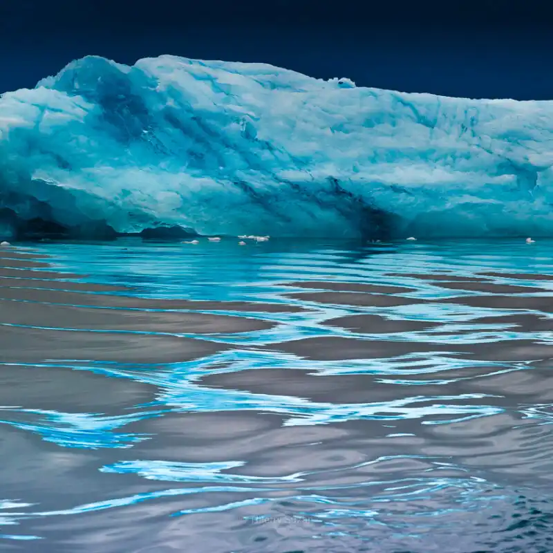 Greenland iceberg with mesmerizing blue arabesque reflections in mirror-calm water