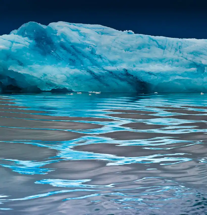 Greenland iceberg with mesmerizing blue arabesque reflections in mirror-calm water