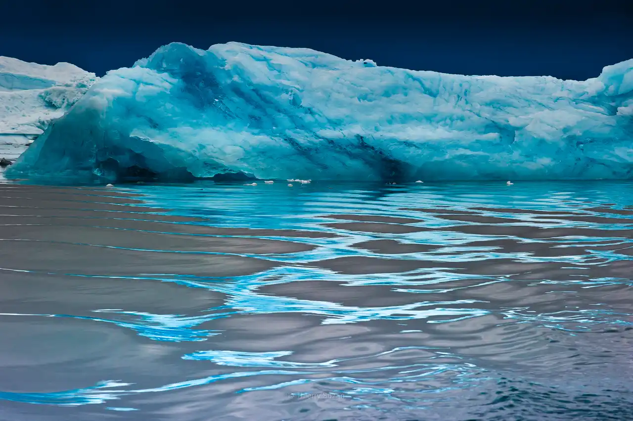 Greenland iceberg with mesmerizing blue arabesque reflections in mirror-calm water