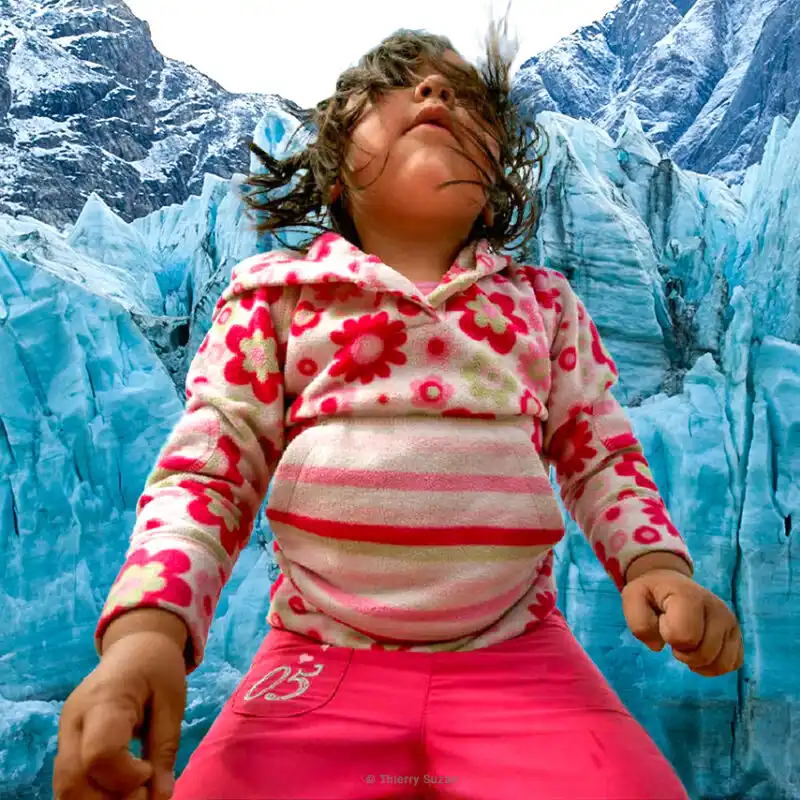 A child with hair blowing in the wind standing before a vast glacier in Greenland