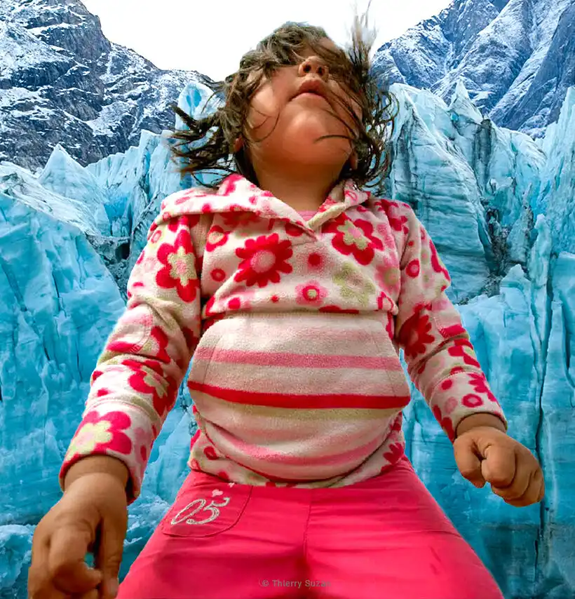 A child with hair blowing in the wind standing before a vast glacier in Greenland
