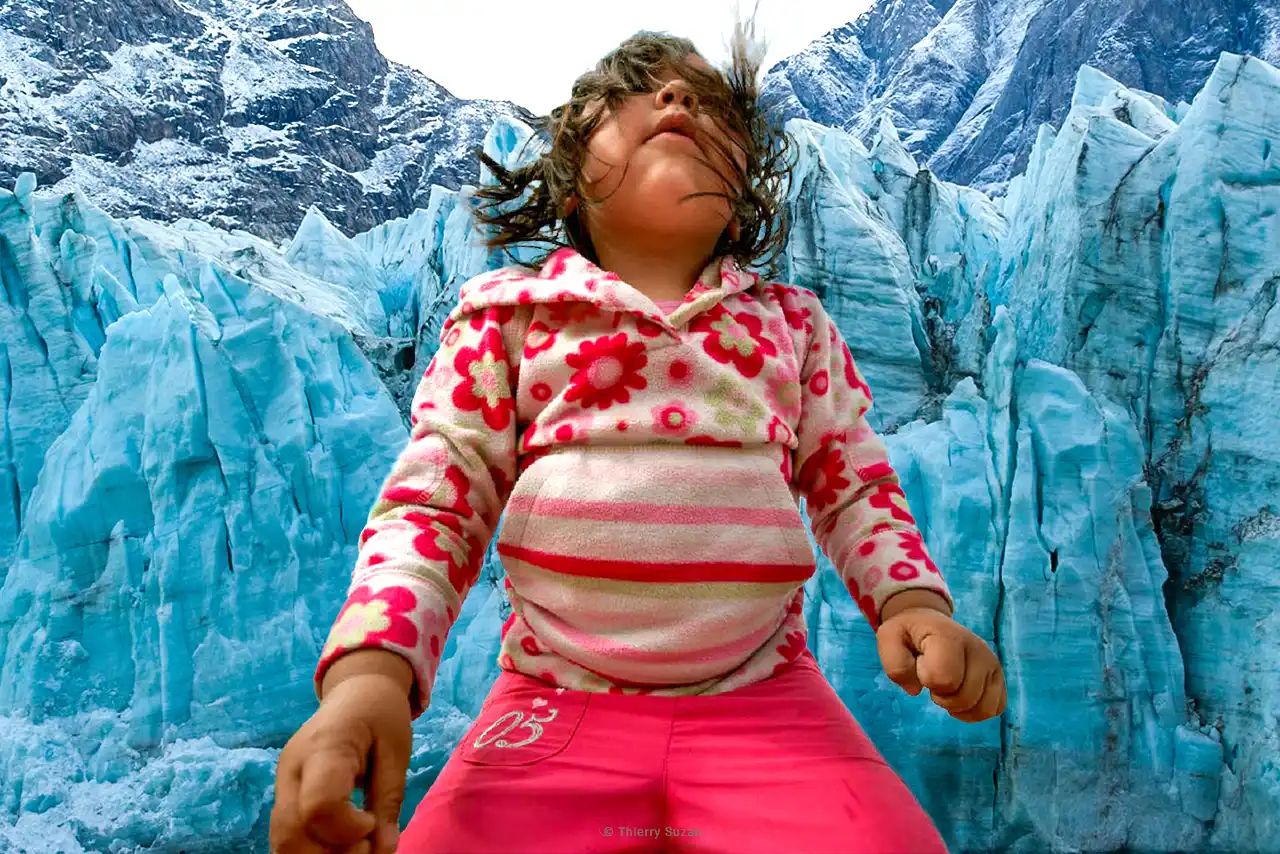 A child with hair blowing in the wind standing before a vast glacier in Greenland