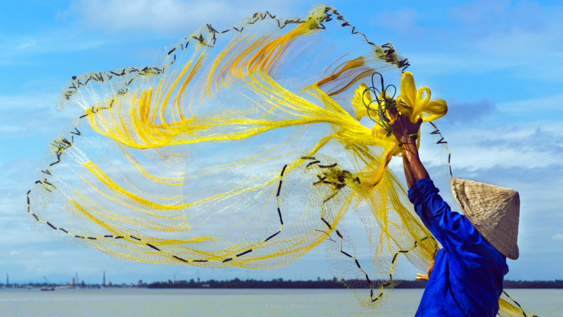 Fisherman casting his net from a boat on the Perfume River, Huế, Vietnam