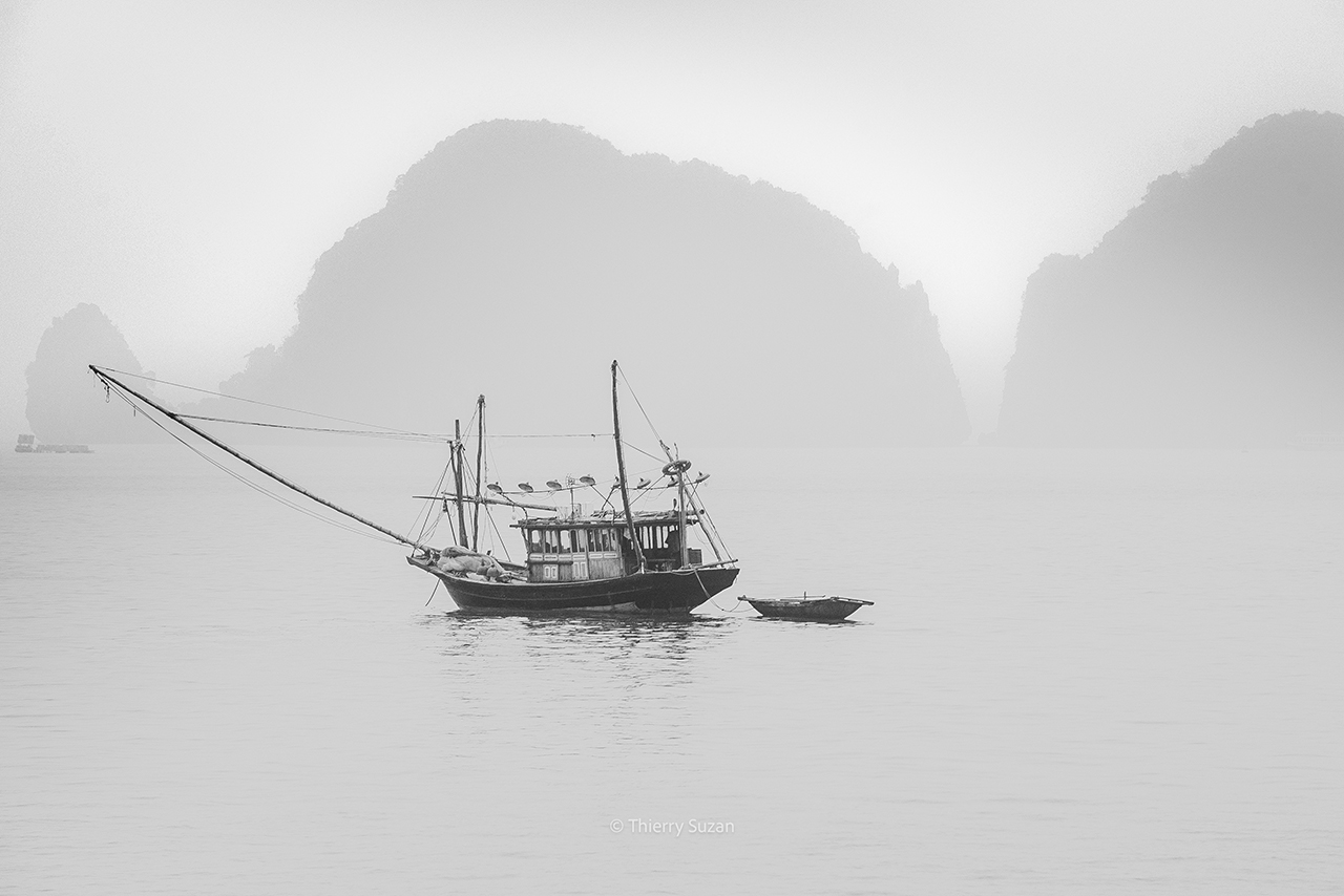 Wooden fishing boat sailing between the karst formations of Ha Long Bay