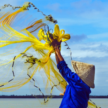 Fisherman casting his net from a boat on the Perfume River, Huế, Vietnam