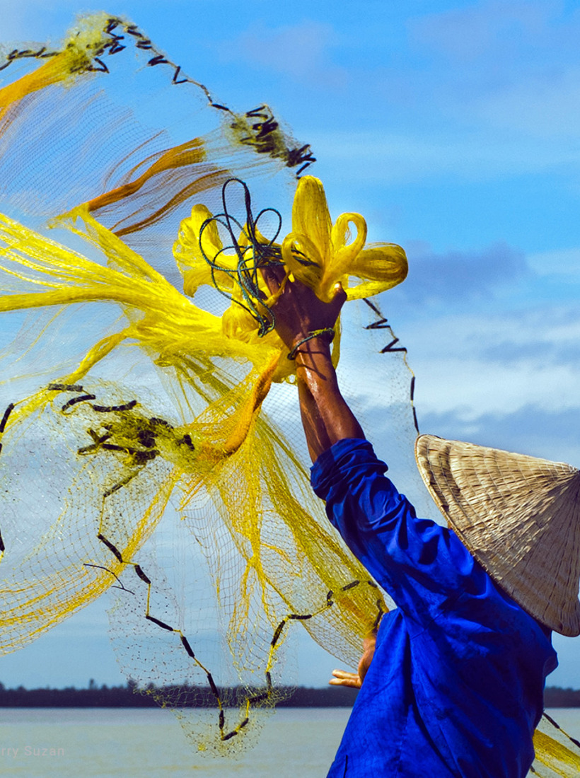 Pêcheur lançant son filet depuis une barque sur la rivière des Parfums à Huế, Vietnam